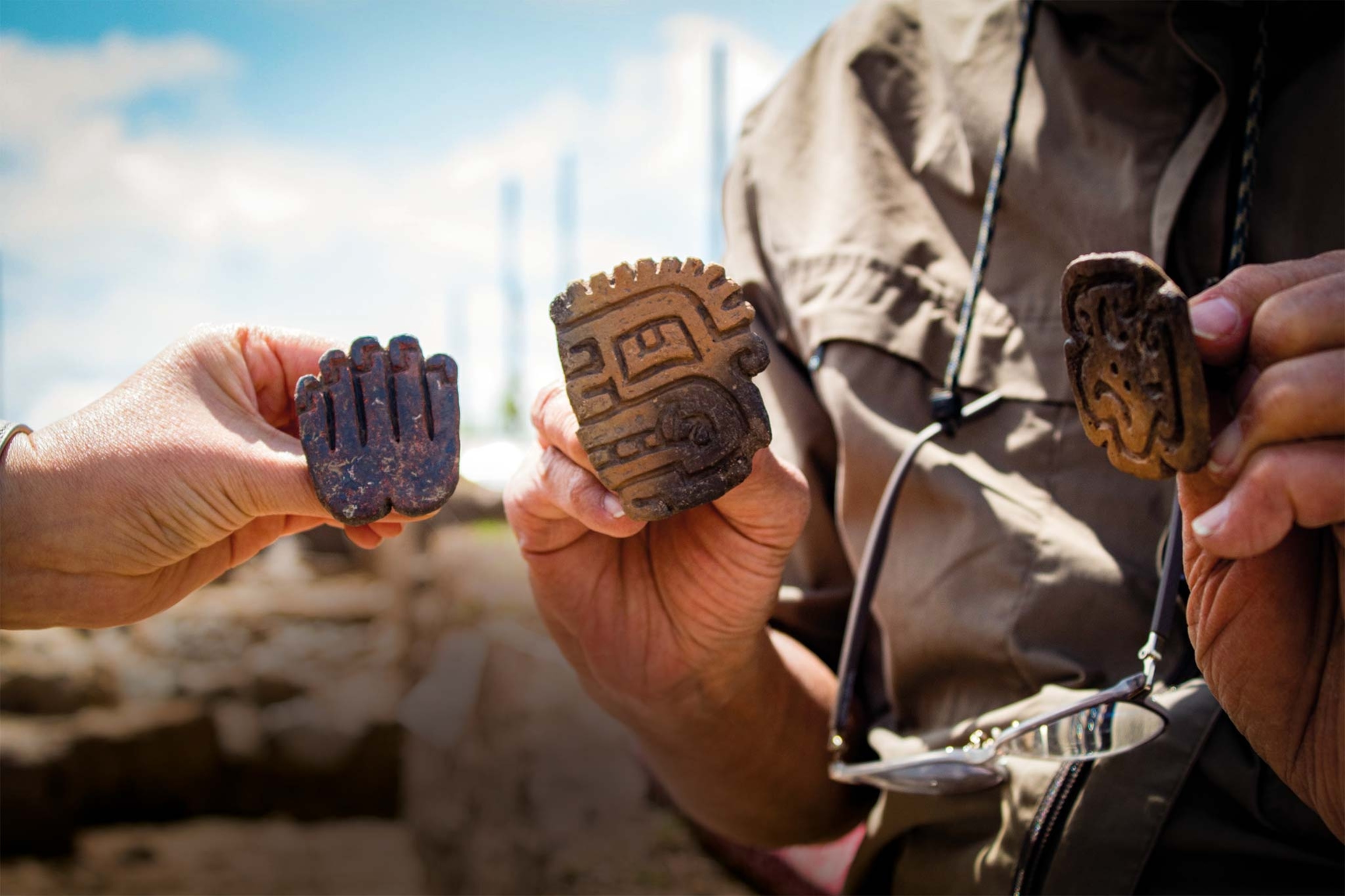 Hands hold up three ceramic seals of a hand, jaguar, and face