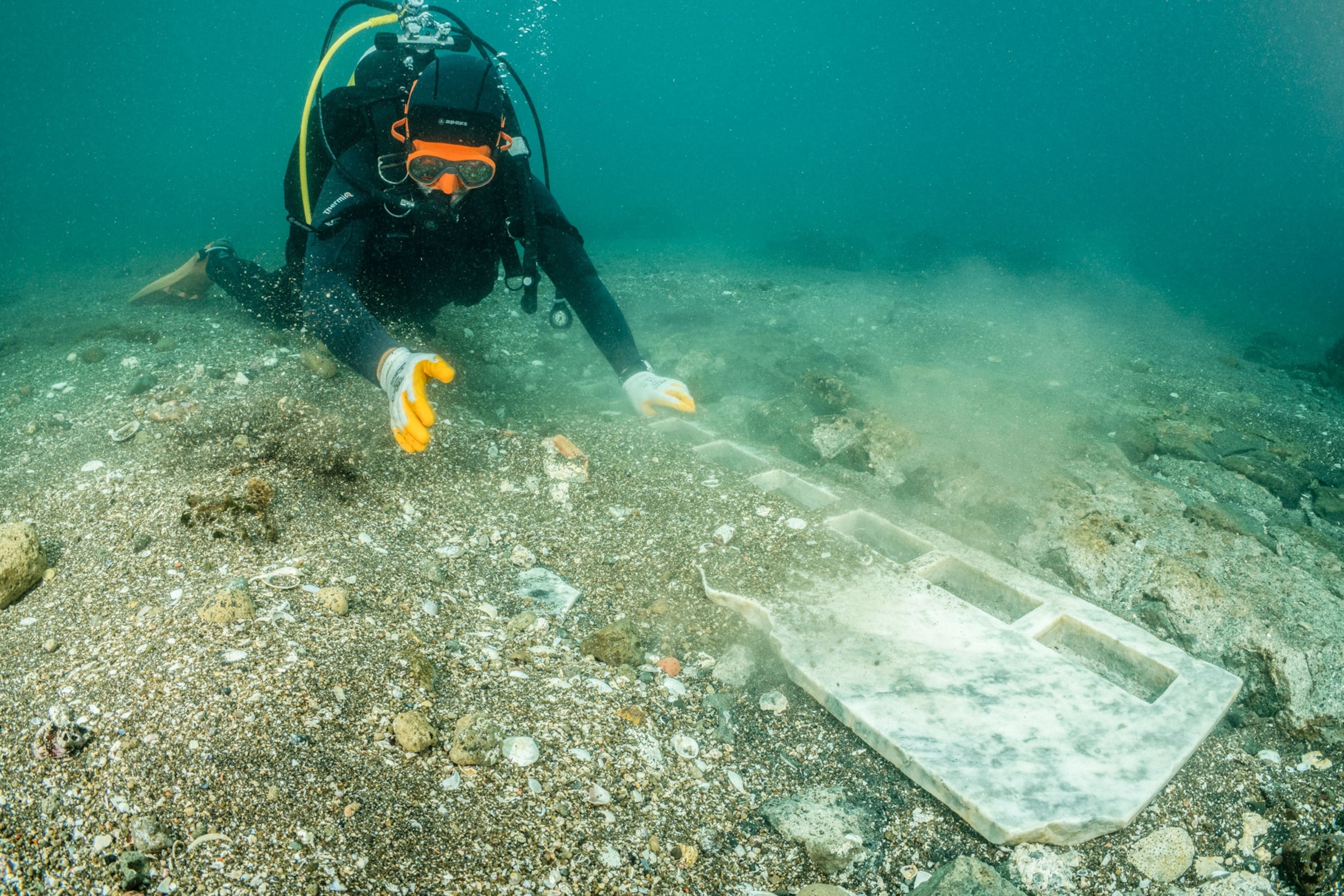 A scuba diver clears rocks and sand off a marble alter found underwater